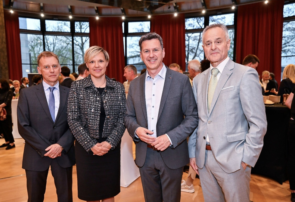 portret štirih oseb, v ozadju stoji več oseb ki se pogovarjajo