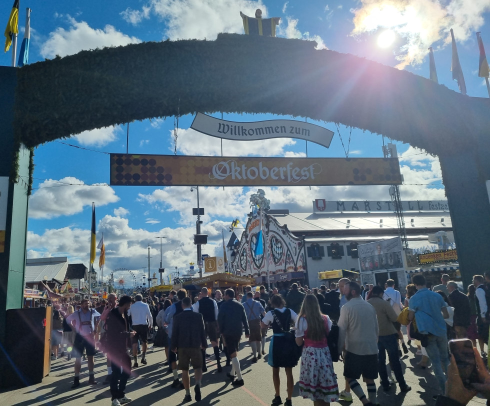 Vhod na Oktoberfest prizorišče. Množica ljudi v bavarskih nošah.