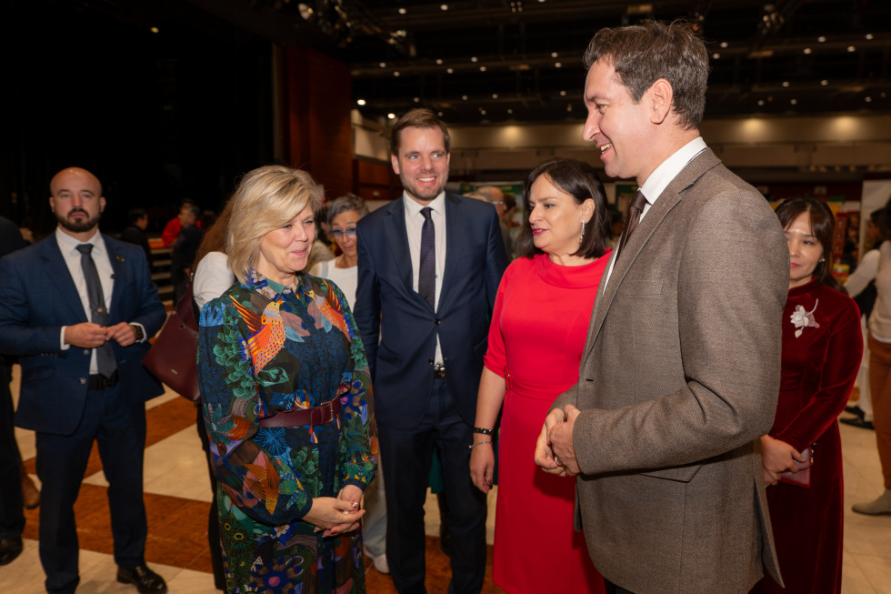 Na fotografiji stoji skupina ljudi, vsi lepo nasmejani. Oseba v barviti obleki se pogovarja z moškim v svetlem suknjiču, ob njiju pa stojita še druga udeleženca v formalnih oblačilih.