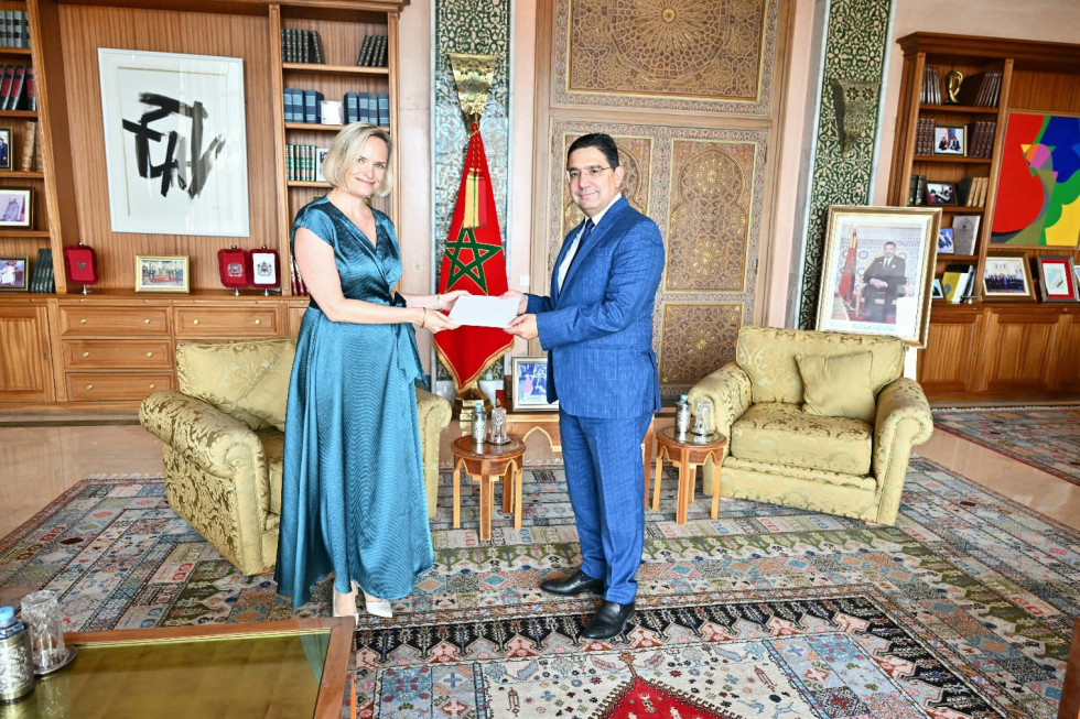 veleposlanica in minister stojita pred zastavami in si predajata mapo