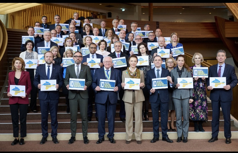 Slika vseh stalnih predstavnikov v predverju stavbe Sveta Evrope, v rokah držijo napise v znak podpore Ukrajini.