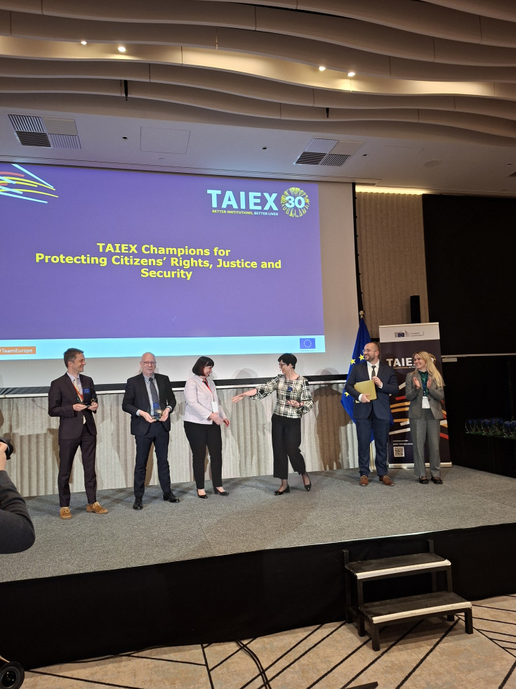 Skupina ljudi stoji na odru ob projekciji predstavitve.