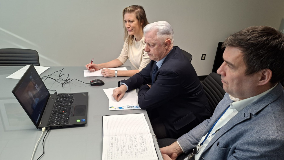 Dva moška in ženska sedijo za mizo, za računalnikom. Spremljajo sestanek.