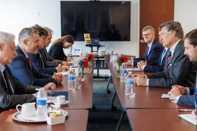 več ljudi, ki sedijo za dolgo  mizo v konferenčni sobi