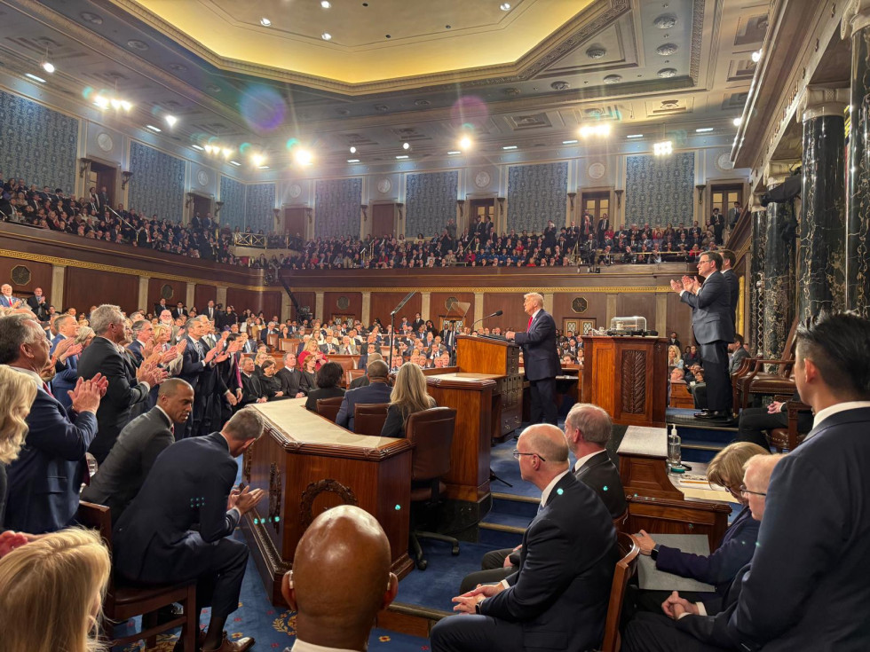 Dvorana polna poslušalcev, ki stojijo in ploskajo. Za govorniškim pultom stoji ameriški predsednik.