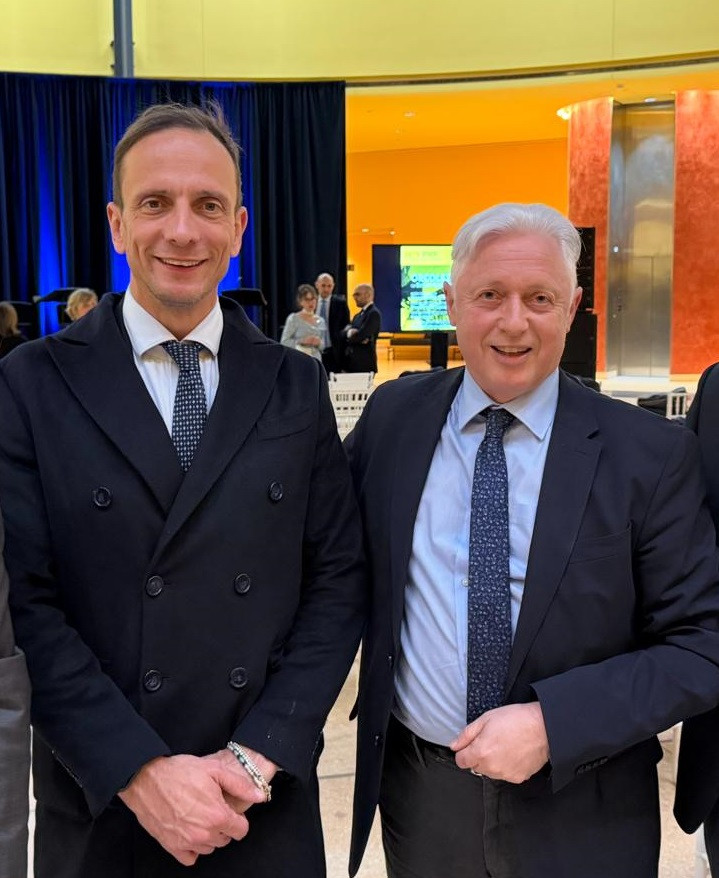 Dva moška v poslovnih oblekah stojita skupaj in pozirata za fotografijo.