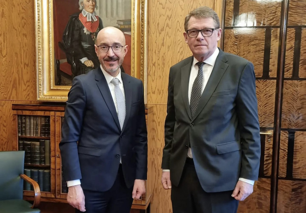 Ambassador and Speaker of the Finnish Parliament standing, looking at the camera, behind them a painting and books