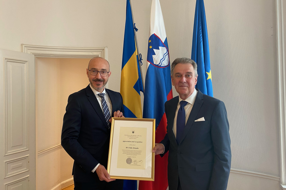 Edvin Skrt is presenting the Recognition Award to Folke Straube, Swedish, Slovenian and EU flags behind then
