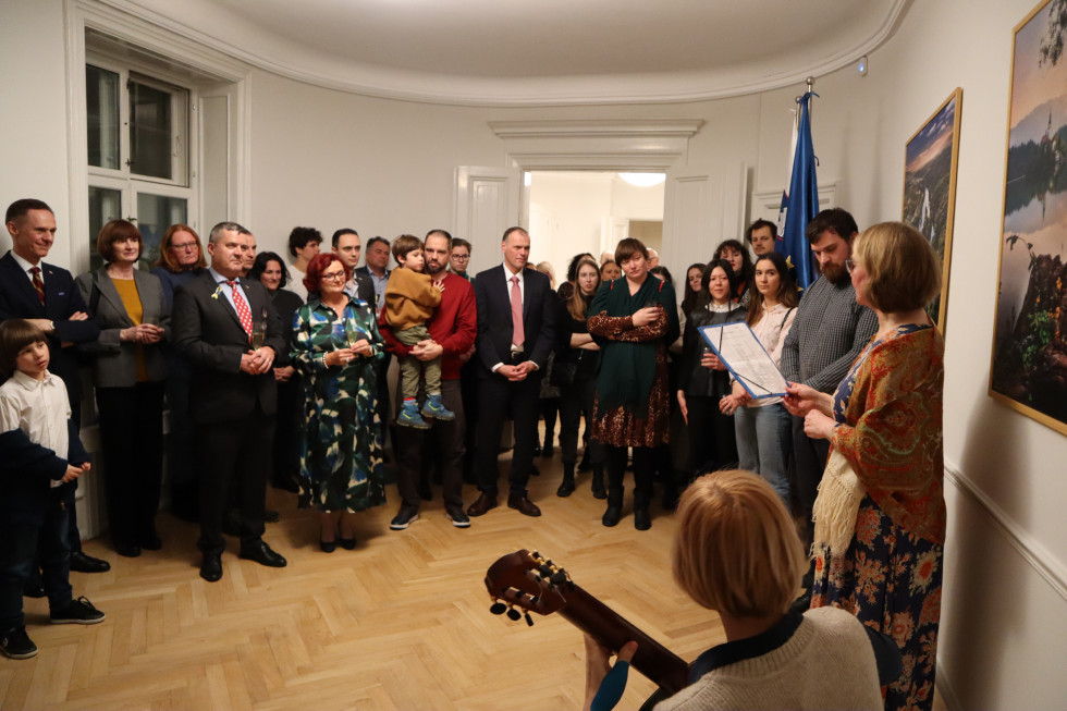 spredaj desno sedi kitaristka Danni, za njo stoji igralka Jette in recitira pesem, v ozadju vidimo množico, ki ju gleda, med njim tudi veleposlanika