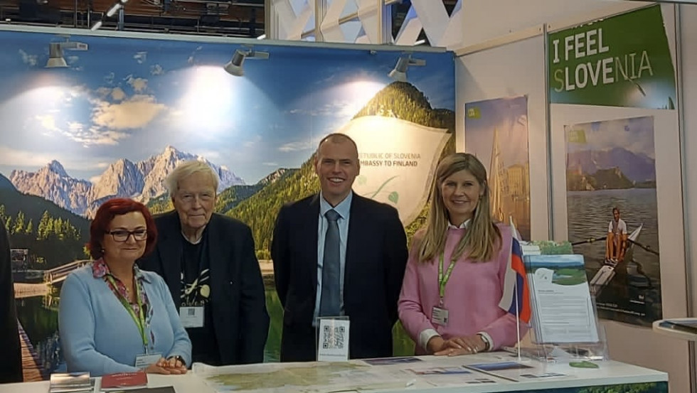 Vsi štirje stojijo v slovenskem paviljonu na sejmu in se smehljajo v kamero, v ozadju so fotografije slovenskih gor