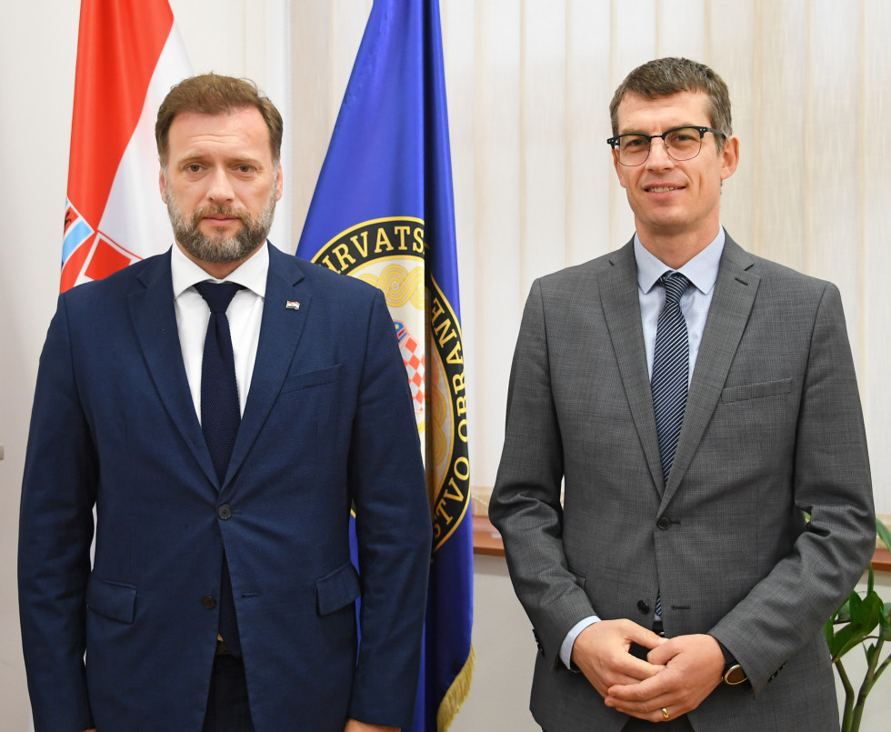 Minister Banožić in veleposlanik Dovžan stojita pred zastavami