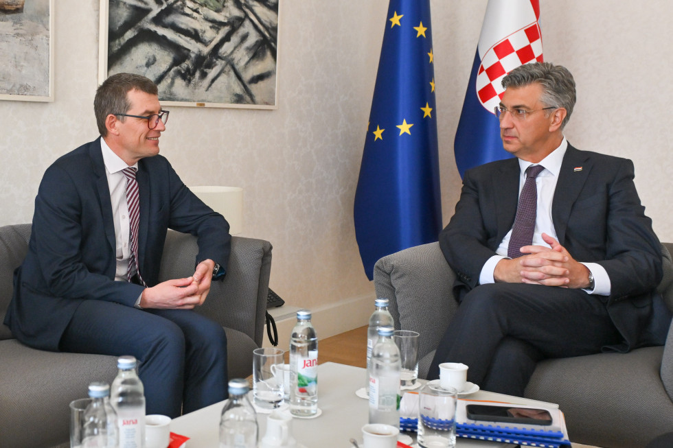 Veleposlanik Dovžan in predsednik Vlade HR Plenković sedita za mizo pred zastavami