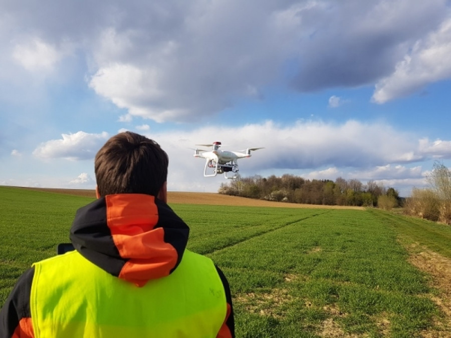 Na fotografiji testiranje z dronom. Oseba ima v rokah napravo in upravlja brezpilotni letalnik. 