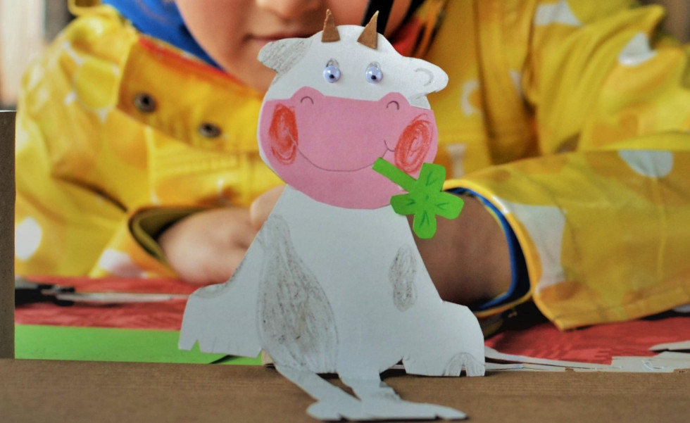 Ročno izdelana papirnata krava v ozadju otrok v rumeni jakni. 