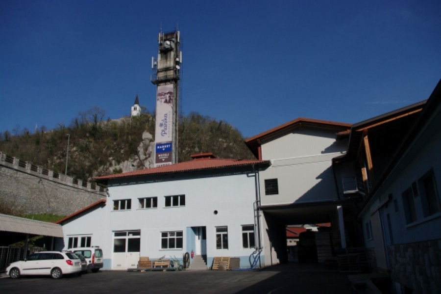 Pogled na poslopje bele barve. Nad njim je velik dimnik. 