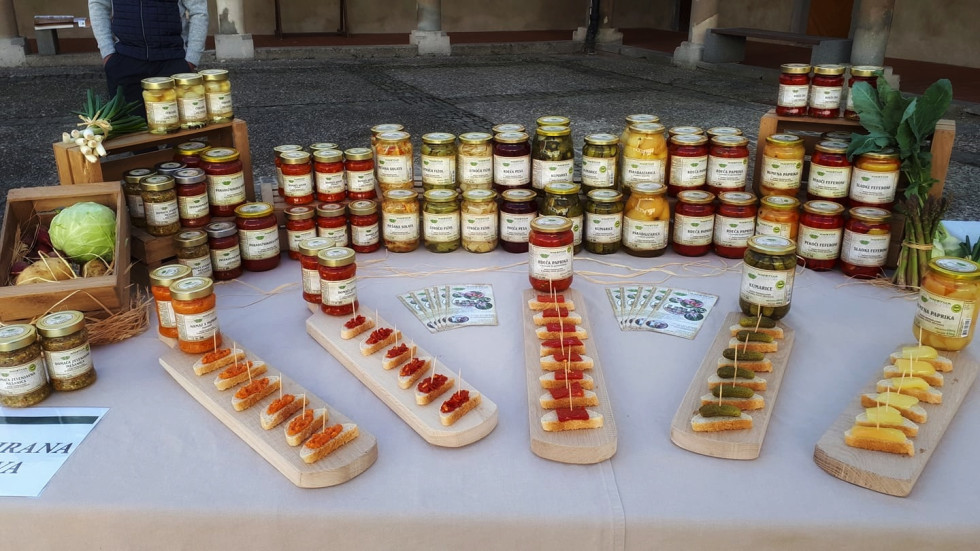 Na tej sliki je prikazan prodajni ali degustacijski prostor, kjer so razstavljeni številni kozarci domačih vložnin ali marmelad, lepo razporejenih v vrstah.