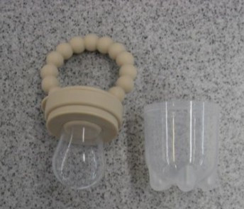 Posodica za hranjenje v obliki dude. Cucelj ima na koncu luknje. Držalo dude je bež barve, cucelj pa je prozoren.