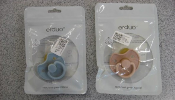 Na sliki sta dve tolažilni dudi, vsaka v svoji embalaži (zip vrečka). Ena duda je roza barve, druga modre barve