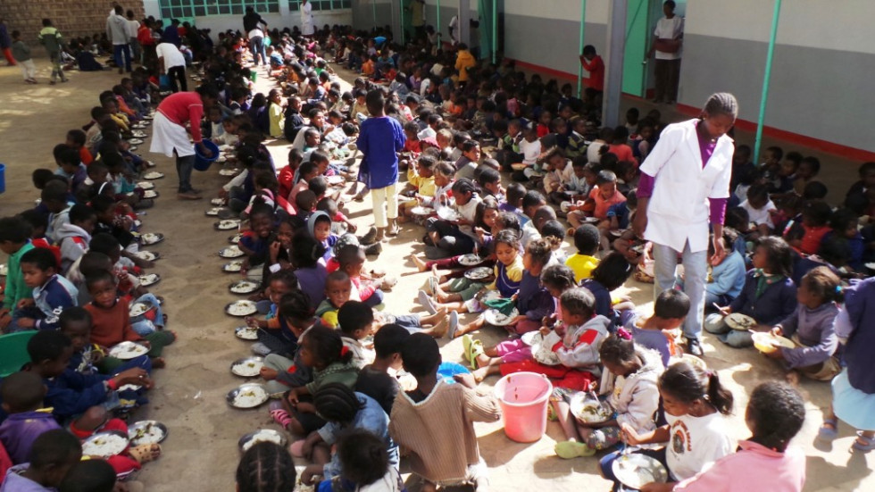 Na dvorišču pred šolo sedi 200 otrok, ki jim učitelji in učenci delijo dnevni obrok šolske prehrane. 