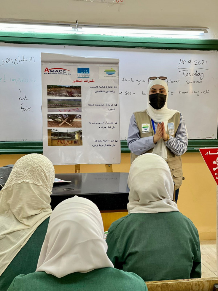  Inštruktorica pred gradivom z vidnim logom MRSHP MZEZ v učilnici predava ženskam o nevarnostih min