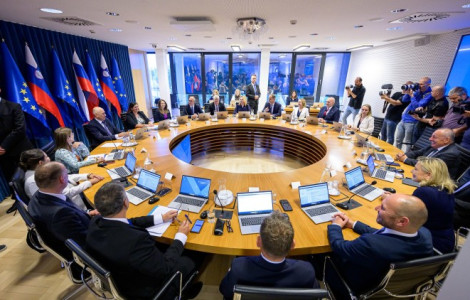1781183794867 (A group of people sitting at a round table with computers in front of them in a room with panoramic windows and slovenian and EU flags.)