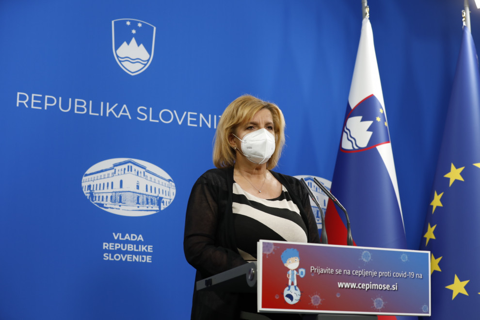Vodja posvetovalne skupine za cepljenje Bojana Beović za govorniškim pultom v sobi za novinarske konference, na desni slovenska zastava.