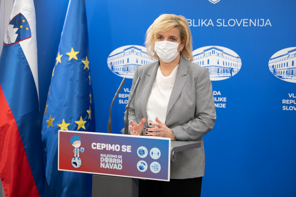 Bojana Beović stoji za govorniškim pultom, na levi sta slovenska in evropska zastava.