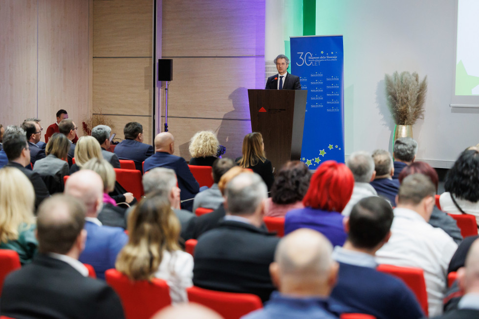 Robert Golob stoji za govornico, v ospredju sedijo udeleženci srečanja.