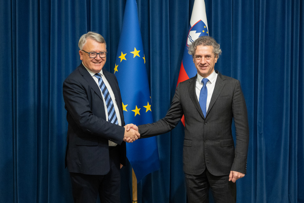 Robert Golob in Nicolas Schmit se rokujeta, v ozadju so zastave.