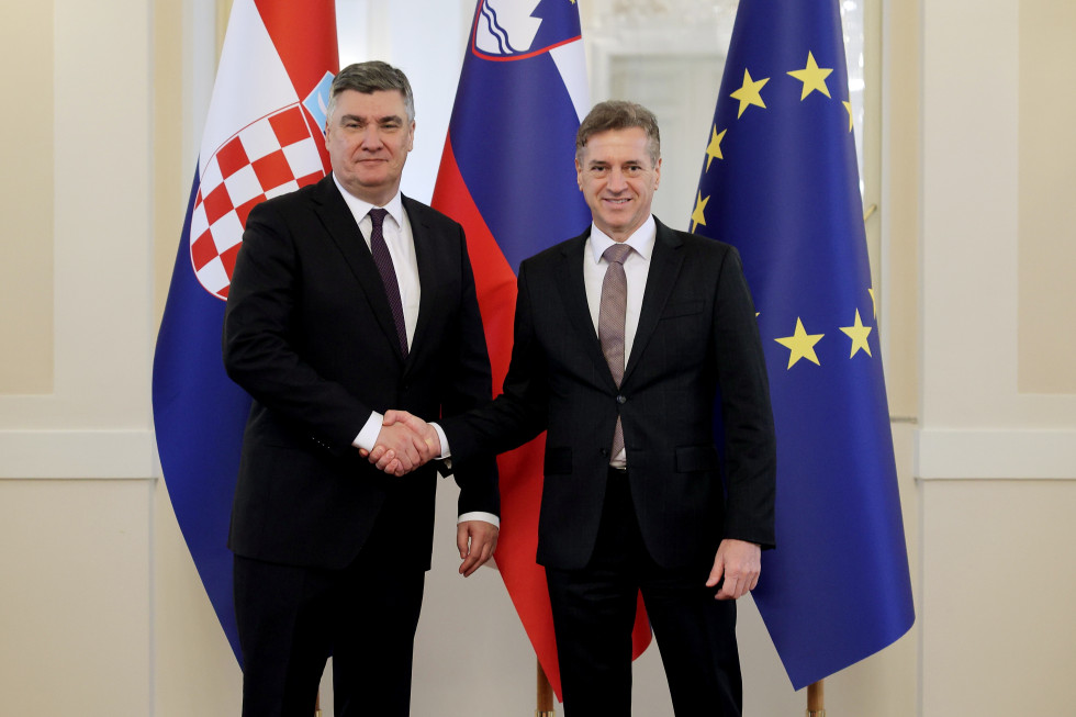 Zoran Milanović in Robert Golob se rokujeta, v ozadju so zastave.