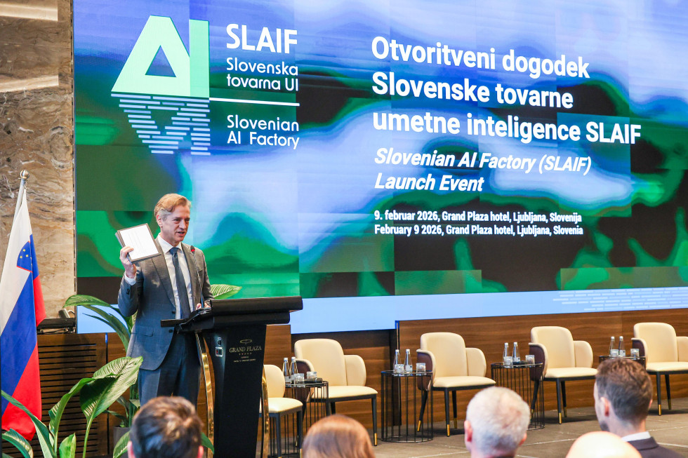 Predsednik vlade za govornico. Zadaj velik ekran z napisom: Otvoritveni dogodek. Slovenske tovarne umetne inteligence SLAIF.