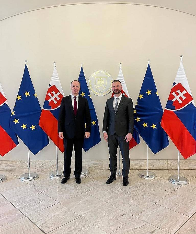 Državni sekretar dr. Andrej Benedejčič in direktor slovaškega urada varnostnega sveta Pavel Franko stojita pred zastavami.