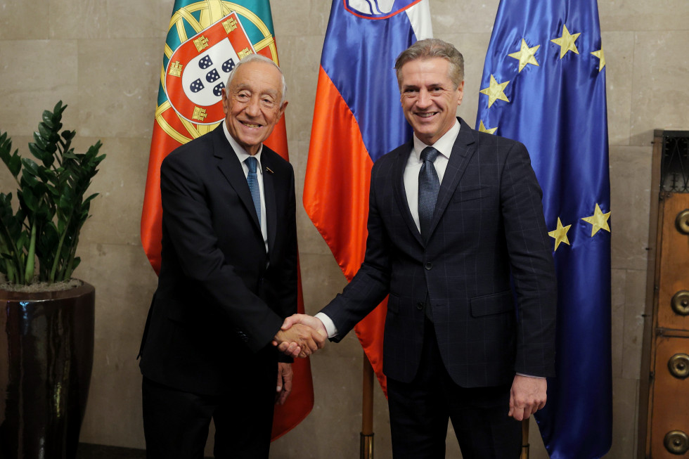 Robert Golob in Marcelo Rebelo de Sousa se rokujeta, v ozadju so zastave.