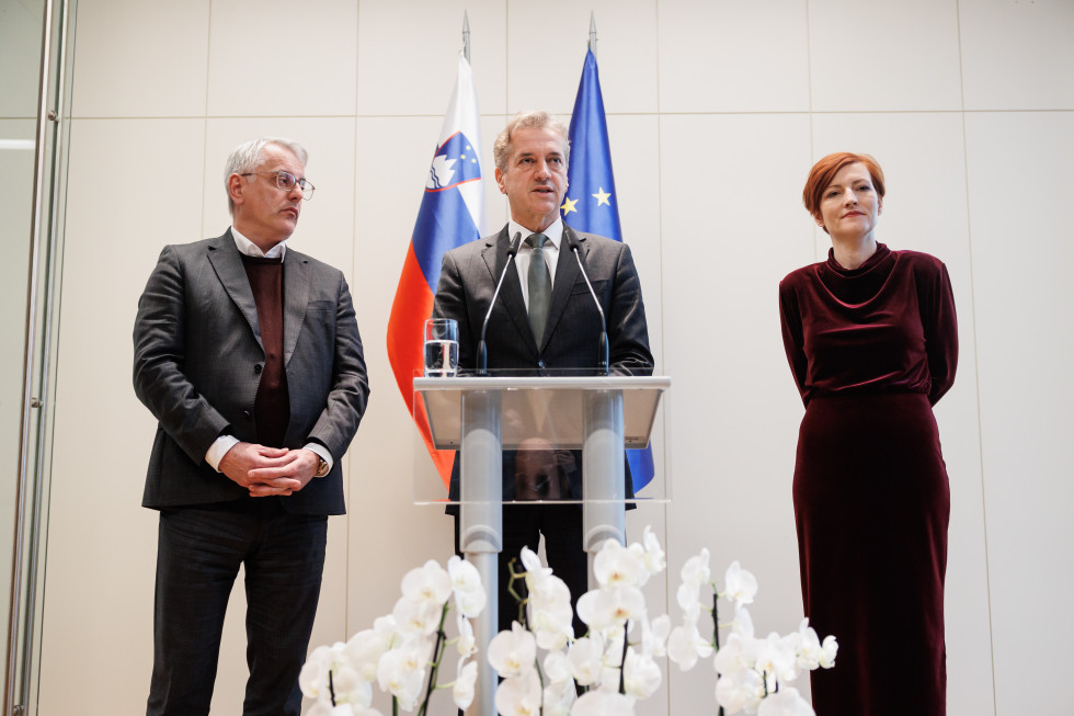 Robert Golob, Matjaž Han in Asta Vrečko stojijo za govornico, v ozadju so zastave, v ospredju so rože.