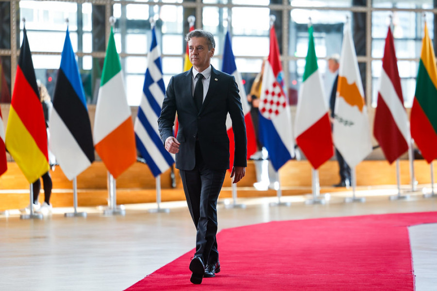 Predsednik vlade prihaja po rdeči preprogi na izredno zasedanje Evropskega sveta; v ozadju zastave držav članic