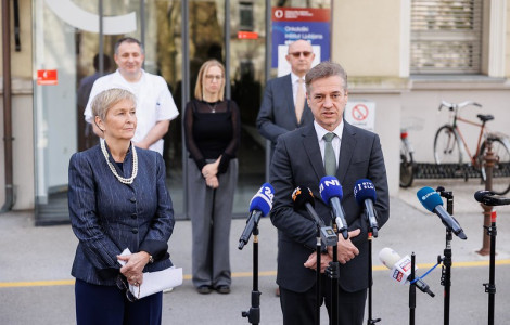 54443211764 9159e160f4 c (A man in a suit speaks at a press conference in front of a healthcare facility, with a woman standing next to him holding a folder, and four colleagues listening in the background.)