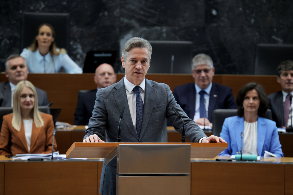 Robert Golob stoji za govornico, v ozadju sedijo članice in člani njegove vlade.