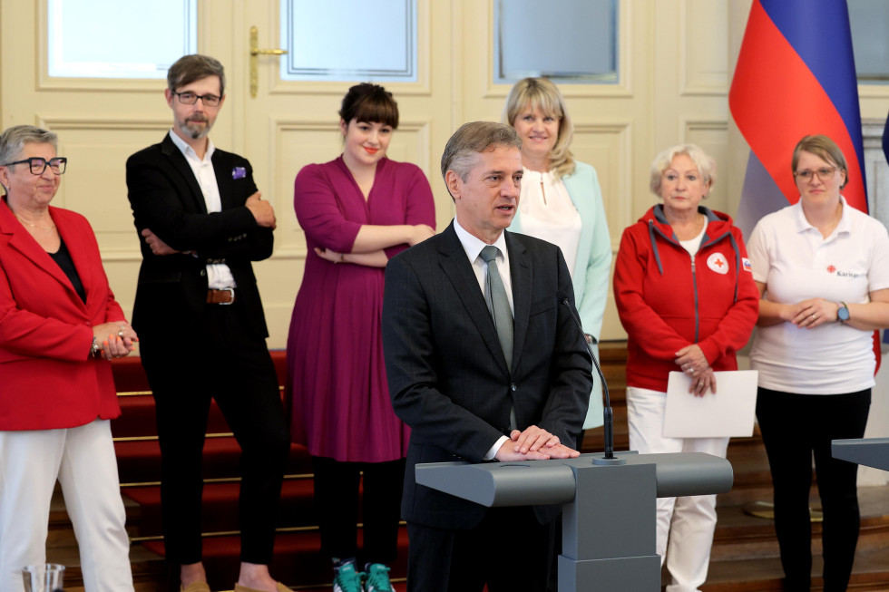 Predsednik vlade za govorniškim pultom, za njim predstavniki socialnih in humanitarnih organizacij
