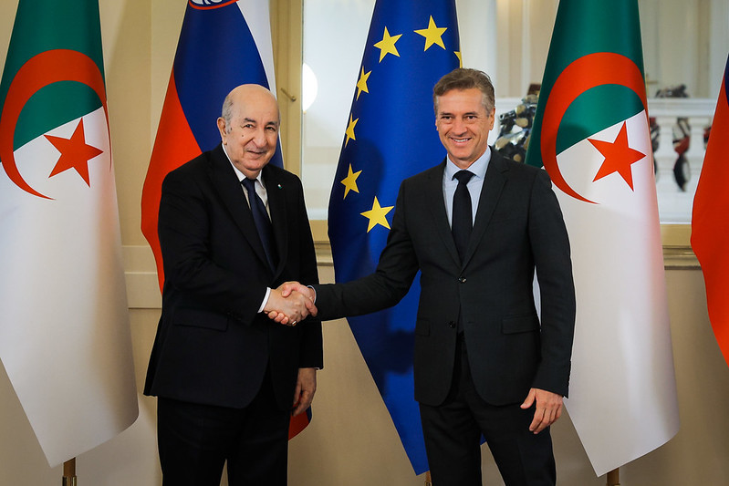 Premier Robert Golob in predsednik Abdelmadjid Tebboune se rokujeta z zastavami Alžirije, Slovenije in EU v ozadju.
