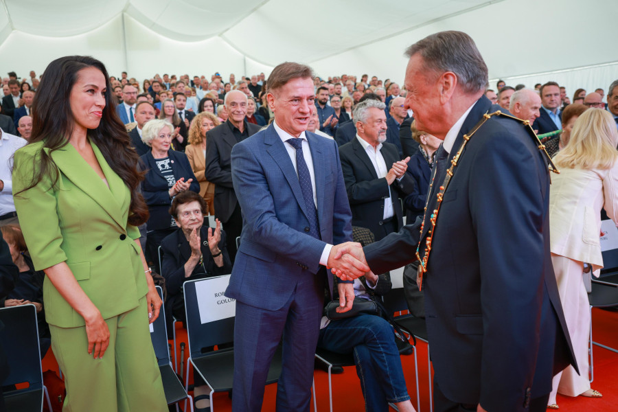 Tina Gaber Golob stoji na levi, Robert Golob in Zoran Janković se rokujeta, v ozadju sedijo udeleženci slavnostne seje.