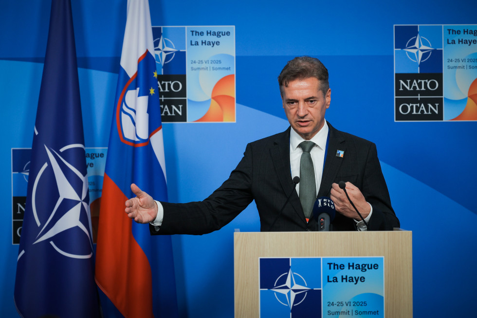 Premier stoji za govorniškim pultom in odgovarja na novinarska vprašanja.