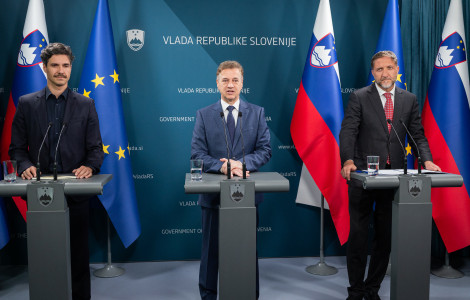 55312006840 4fbaaf2e2b k (Three men stand behind podiums during a press conference at the Government of Slovenia, with Slovenian and EU flags in the background.)