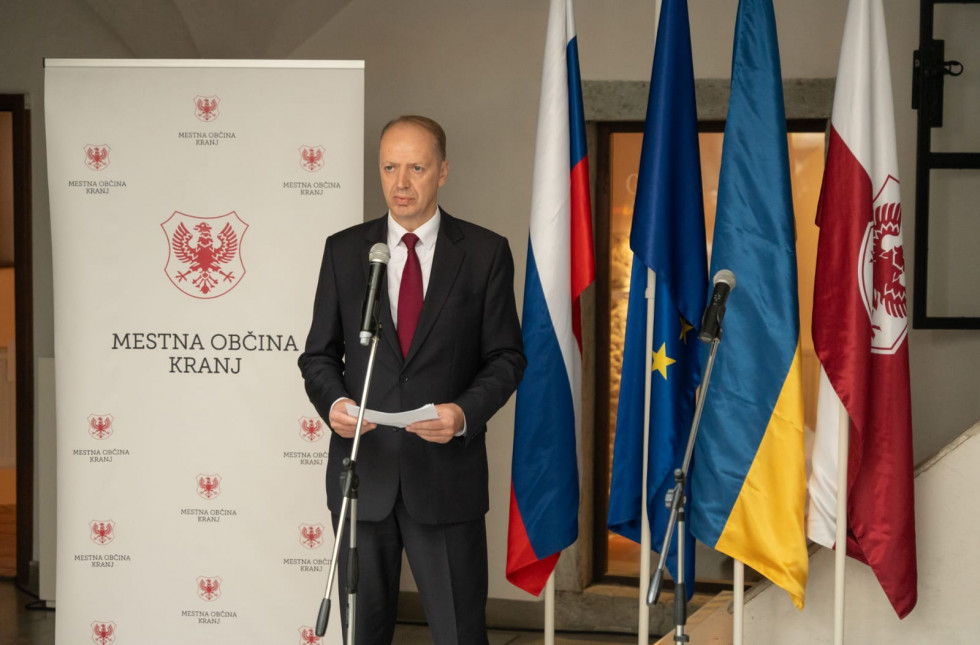  Andrej Benedejčič stands behind the microphone, with flags next to him.