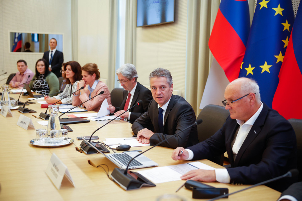 Predsednik vlade Robert Golob in člani sveta sedijo za mizo v sejni dvorani.