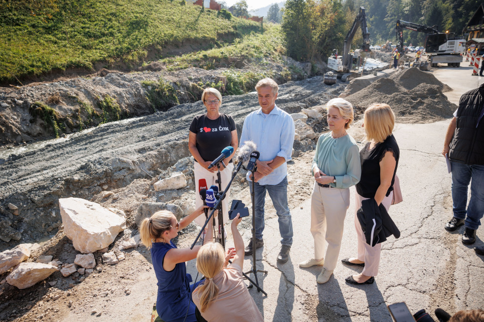 The Prime Minister, the President of the European Commission and the Mayor of Črna na Koroškem stand in front of the journalists' microphones at the road reconstruction section. Behind them are piles of sand and construction machinery and workers.