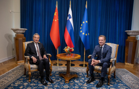 Kitajska (The two men are sitting opposite each other, with a small round table between them. In the background, there are flags.)