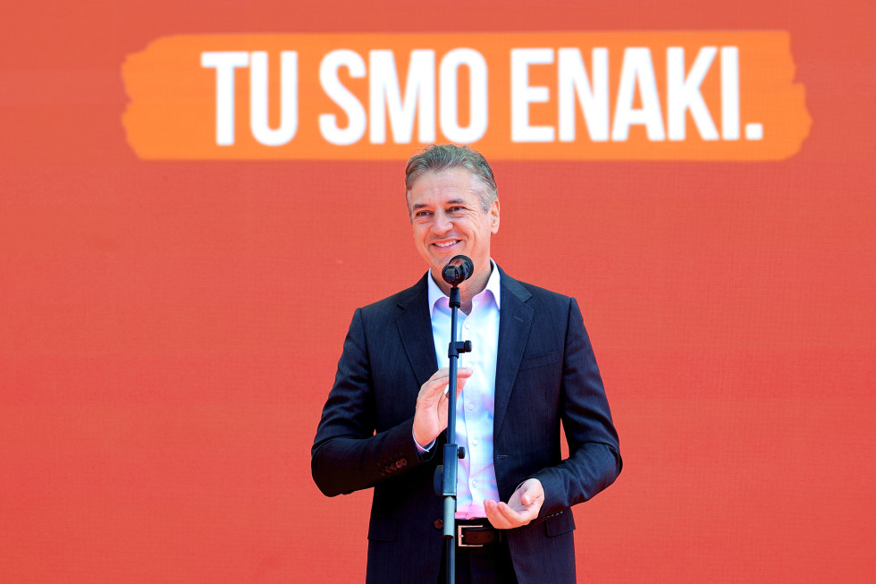 The prime minister stands behind the microphone and is smiling. In the background, there is a sign that says We are equal here.