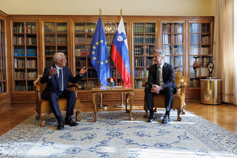 Dr. Robert Golob and António Costa are seated and engaged in conversation. Behind them is a beautiful bookshelf, along with the Slovenian and European flags.