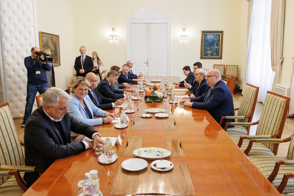The participants of the meeting are seated at a table set with plates and glasses.