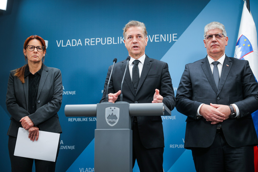 Andreja Katič, Robert Golob in Boštjan Poklukar stojijo za govornicami, v ozadju so oznake slovenske vlade.